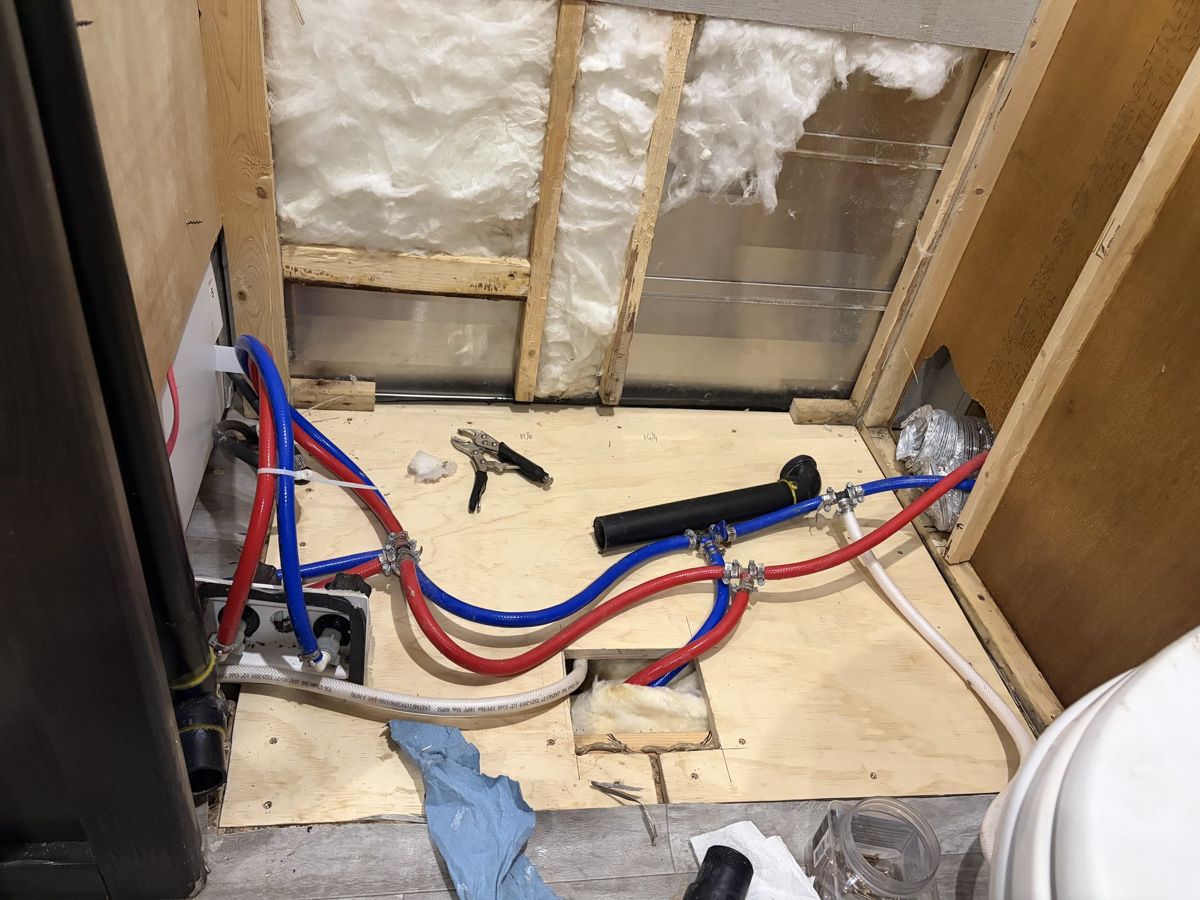 RV bathroom wall opened up showing red and blue PEX water lines